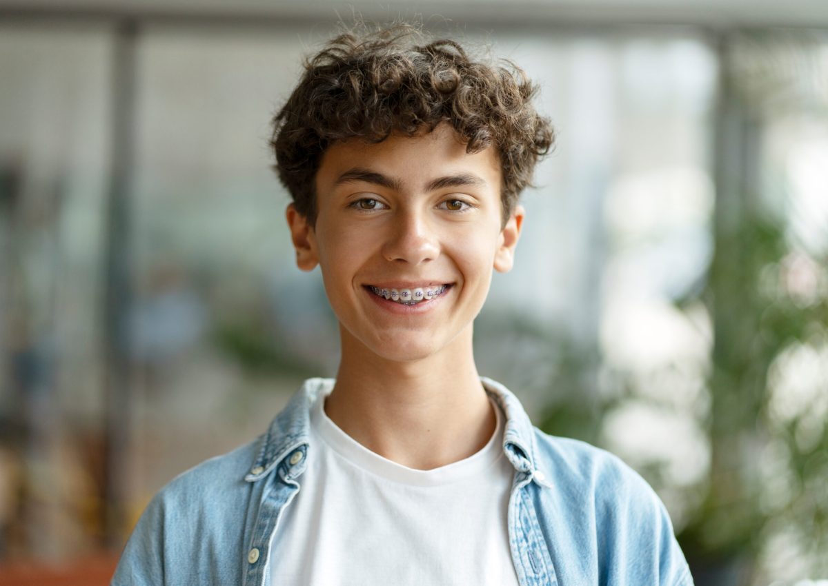 Closeup portrait of smiling smart curly haired school boy wearing braces on teeth looking at camera. Education concept