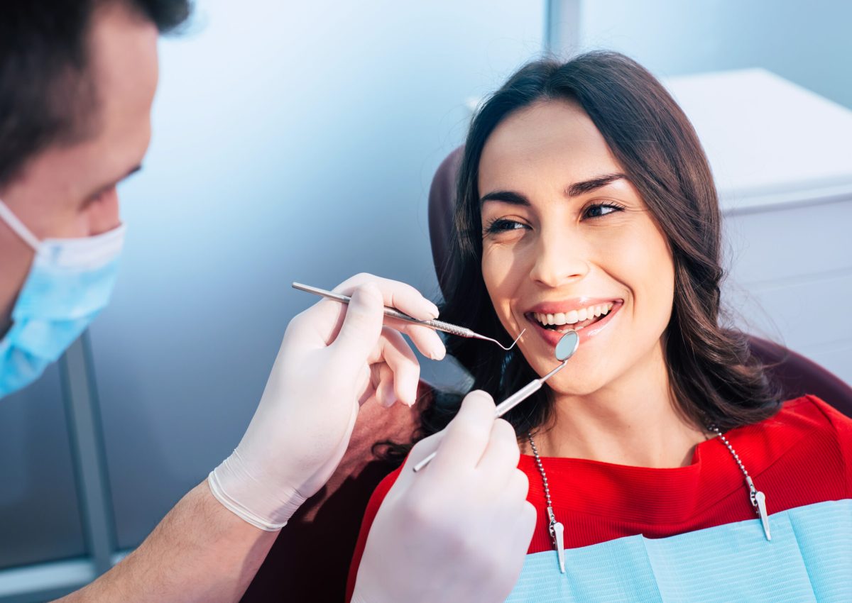Wonderful treatment. Dentist in ear loop face mask and gloves is holding dental instruments and checking the result of his professional work in the dental center.