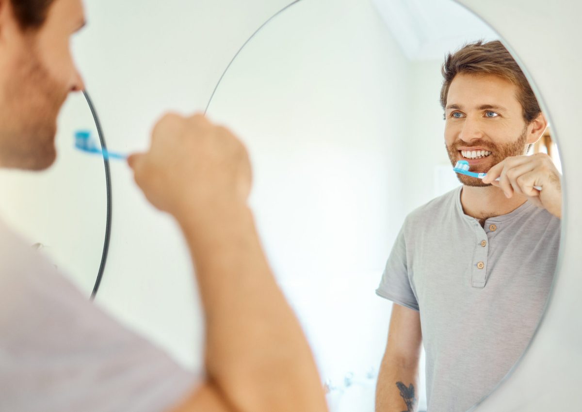 Brushing teeth, dental and mirror with man in bathroom for self care, oral hygiene and morning routine. Cleaning, smile and health with face of male person at home for beauty, wellness and toothbrush.