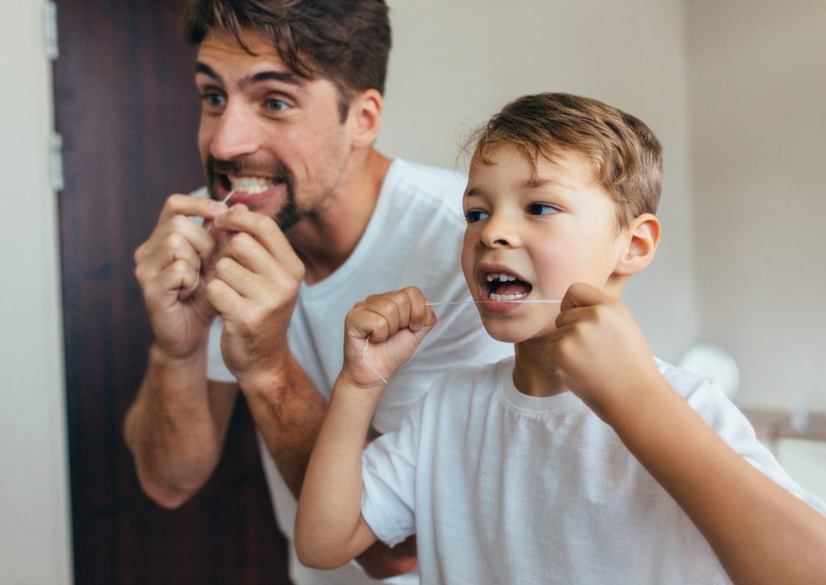 Little boy with his father in bathroom cleaning teeth with dental floss. Both looking in mirror and brushing teeth.