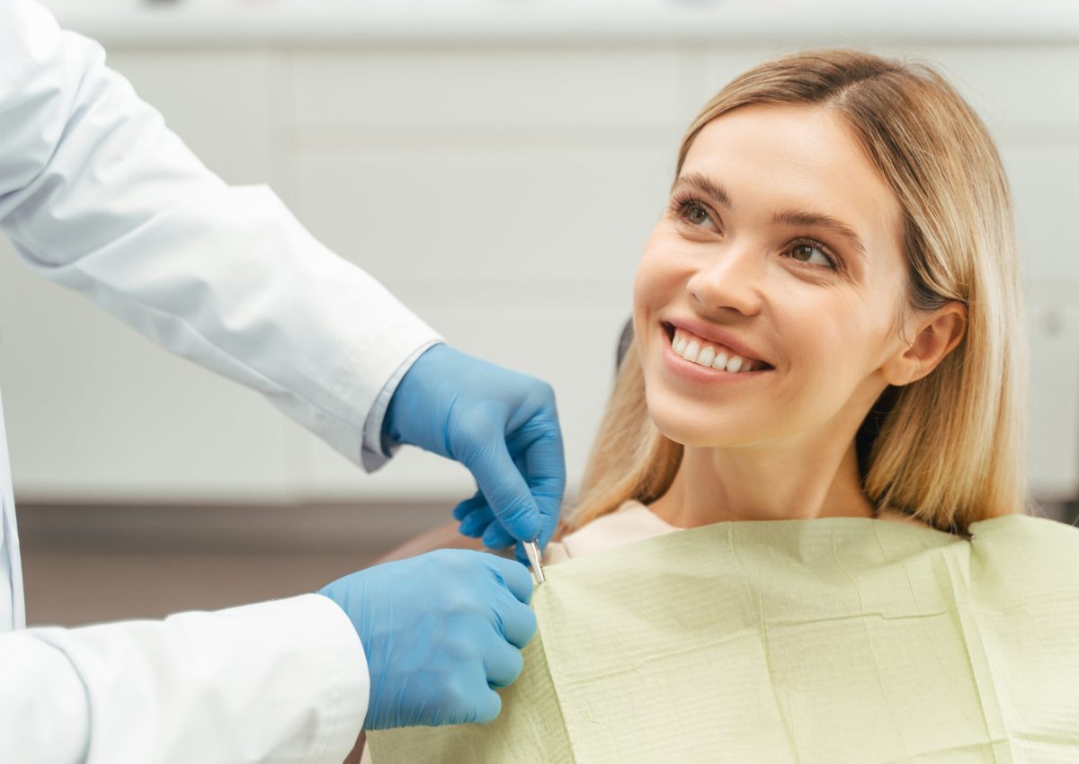 Portrait of smiling beautiful female patient with blond hair sitting in dental chair. Attractive young woman visiting modern clinic. ?oncept of dental care